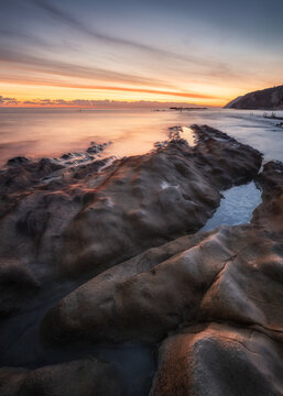 View of the Sedia del Papa rock formation at Passetto beach during a golden sunset with calm water and rocky coastline in Ancona, Marche, Italy.