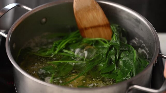 Blanching fresh green spinach in a pot of boiling water and stirring with wooden spatula, preparing ingredients for Korean spinach salad (Sigeumchi namul)