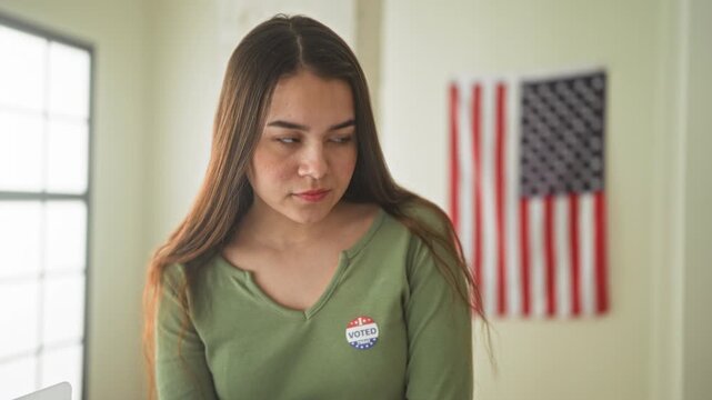 Woman wearing a voted sticker at a polling booth looking down while placing a ballot in a building; civic duty pride participation.