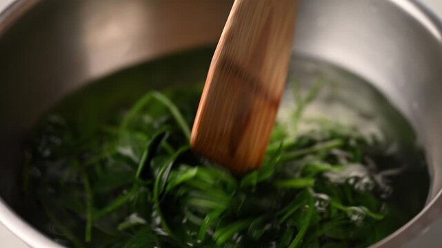 Transferring blanched spinach into a bowl of cold water, cooling process for Korean spinach salad (Sigeumchi namul)