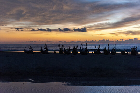 View of traditional fishing boats silhouetted against a vibrant sunset sky on the sandy shore of Inani Beach, Cox's Bazar District, Chittagong Division, Bangladesh.