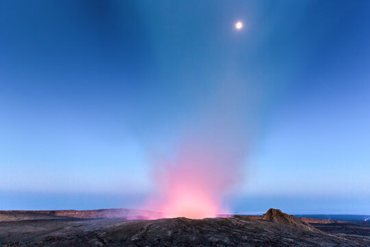 View of the glowing lava lake of Erta Ale volcano under a twilight sky with a visible moon.