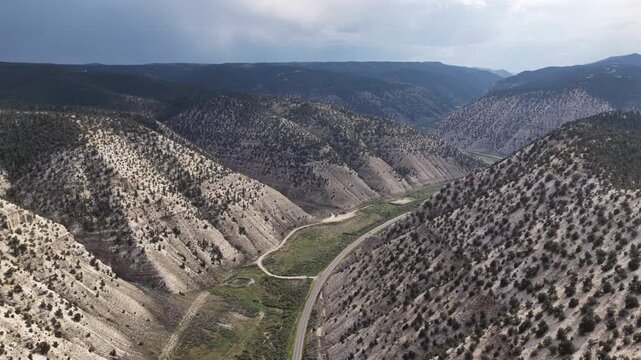 Aerial of canyon and winding road through scrubland mountain slopes with paved highway following the valley floor surrounded by steep in Duchesne Utah