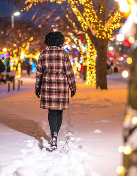 Winter snow woman coat plaid curly hair city street night light holiday festive sidewalk tree decoration snowflake park footstep boot warm jacket seasonal outdoor urban walking Christmas Concept