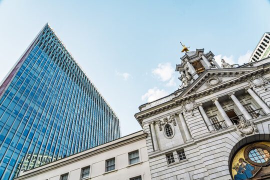View of the historic Old Bailey courthouse facade with its golden statue of Justice, contrasted against a modern glass skyscraper under a clear blue sky in London, England, United Kingdom.