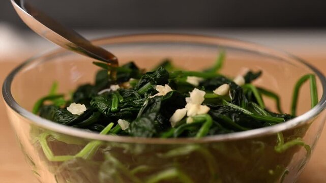Pouring sesame oil into mixing bowl with Korean spinach salad (Sigeumchi namul), slow motion