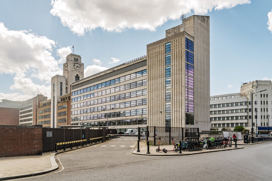 View of the historic Victoria Coach Station building with its prominent clock tower, modern glass windows, and a row of parked rental scooters in London, England, United Kingdom.