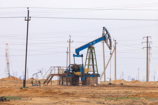 View of an industrial oil pumpjack operating in an oil field with power lines and desert terrain in Zhanaozen, Mangystau Region, Kazakhstan.