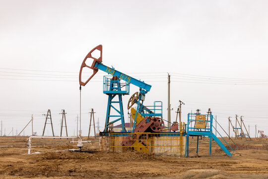 View of an oil pump jack operating in an oil field with power lines and a barren landscape in Zhanaozen, Mangystau Region, Kazakhstan.