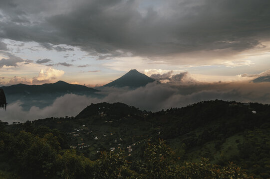 View of the volcanic landscape near Antigua Guatemala with clouds rolling over the peaks at sunset, Antigua Guatemala, Sacatepequez Department, Guatemala.