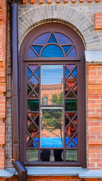 An elegant stone arched window with a wooden frame and colored glass. A wall made of red brick, a sunny day.