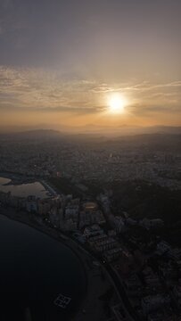 Aerial view of Malaga bullring (Plaza de Toros de la Malagueta) illuminated at sunset. Cinematic drone shot of the coastal arena, Mediterranean sea, and city skyline during golden hour.