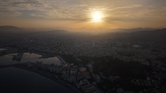 Aerial view of Malaga bullring (Plaza de Toros de la Malagueta) illuminated at sunset. Cinematic drone shot of the coastal arena, Mediterranean sea, and city skyline during golden hour.