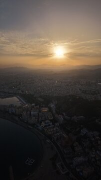 Aerial view of Malaga bullring (Plaza de Toros de la Malagueta) illuminated at sunset. Cinematic drone shot of the coastal arena, Mediterranean sea, and city skyline during golden hour.
