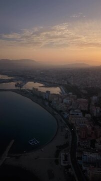 Aerial view of Malaga bullring (Plaza de Toros de la Malagueta) illuminated at sunset. Cinematic drone shot of the coastal arena, Mediterranean sea, and city skyline during golden hour.