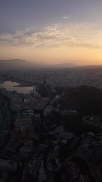 Aerial view of Malaga bullring (Plaza de Toros de la Malagueta) illuminated at sunset. Cinematic drone shot of the coastal arena, Mediterranean sea, and city skyline during golden hour.