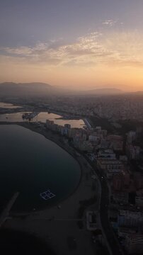 Aerial view of Malaga bullring (Plaza de Toros de la Malagueta) illuminated at sunset. Cinematic drone shot of the coastal arena, Mediterranean sea, and city skyline during golden hour.