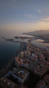 Aerial view of Malaga bullring (Plaza de Toros de la Malagueta) illuminated at sunset. Cinematic drone shot of the coastal arena, Mediterranean sea, and city skyline during golden hour.