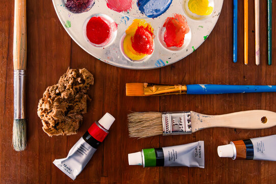 Art supplies laid out on a table: paint, brushes, palette, sponge