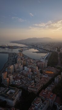 Aerial view of Malaga bullring (Plaza de Toros de la Malagueta) illuminated at sunset. Cinematic drone shot of the coastal arena, Mediterranean sea, and city skyline during golden hour.