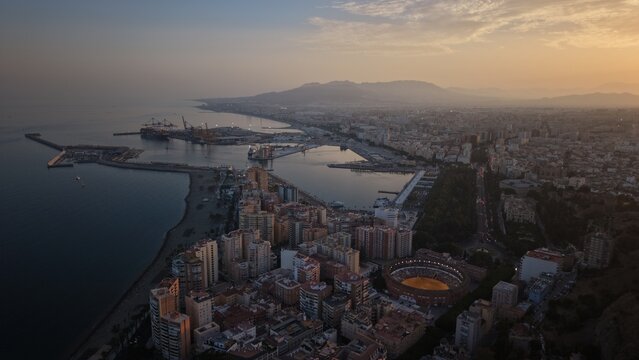 Aerial view of Malaga bullring (Plaza de Toros de la Malagueta) illuminated at sunset. Cinematic drone shot of the coastal arena, Mediterranean sea, and city skyline during golden hour.