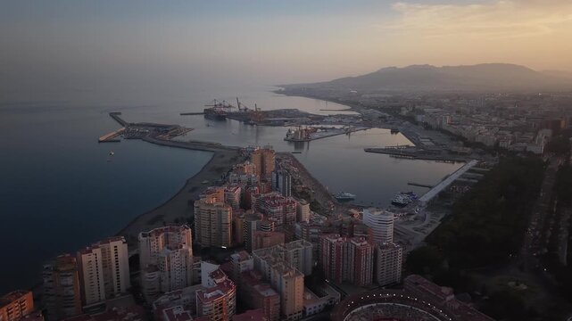 Aerial view of Malaga bullring (Plaza de Toros de la Malagueta) illuminated at sunset. Cinematic drone shot of the coastal arena, Mediterranean sea, and city skyline during golden hour.