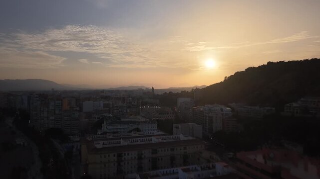 Aerial view of Malaga bullring (Plaza de Toros de la Malagueta) illuminated at sunset. Cinematic drone shot of the coastal arena, Mediterranean sea, and city skyline during golden hour.