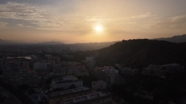 Aerial view of Malaga bullring (Plaza de Toros de la Malagueta) illuminated at sunset. Cinematic drone shot of the coastal arena, Mediterranean sea, and city skyline during golden hour.