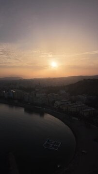 Aerial view of Malaga bullring (Plaza de Toros de la Malagueta) illuminated at sunset. Cinematic drone shot of the coastal arena, Mediterranean sea, and city skyline during golden hour.