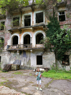 Young girl standing in front of an overgrown abandoned building in city of Akarmara, Abkhazia. Child exploring old ruined architecture with arched windows and ivy. Urban exploration concept
