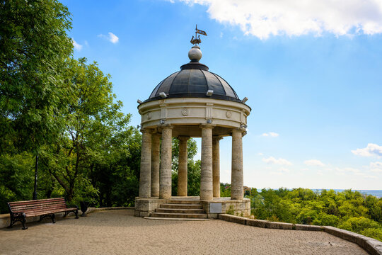 Stone rotunda with a domed roof in a green park in Pyatigorsk, Russia. Classic gazebo architecture on a paved viewpoint overlooking a landscape.