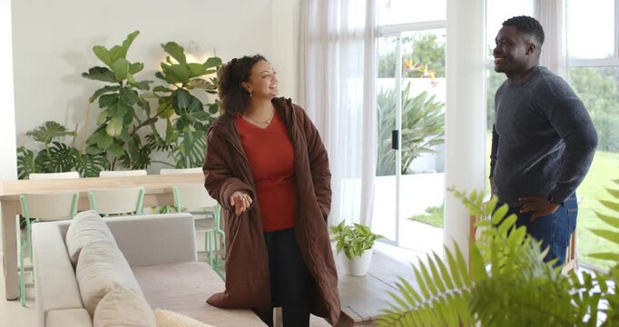 Couple near glass doors with woman gesturing, holding remote and showing room while man watching