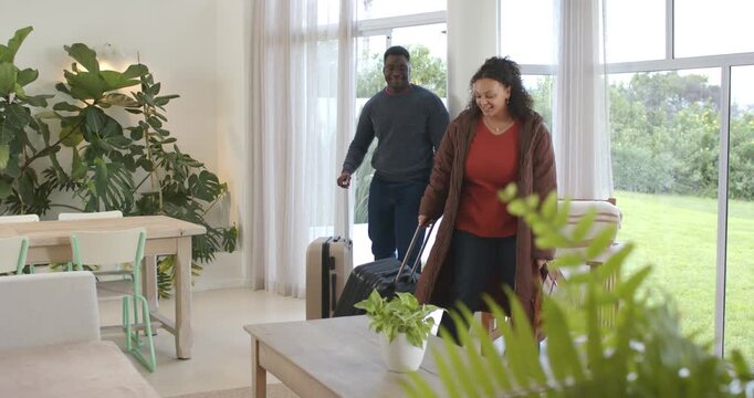 African American couple arriving via glass door pulling cases placing bag looking at living area