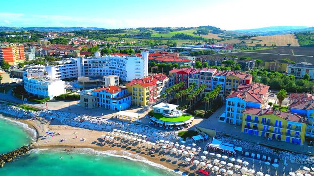 PORTO RECANATI, ITALY - JULY 30, 2025: Aerial pullback tilt up shot from Porto Recanati. The unusual, colored buildings by the promenade surrounded by the Adriatic Sea and soothing Marche hillscapes