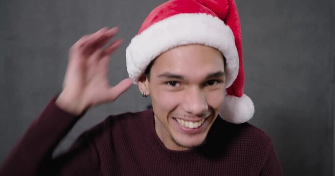 African American man smiling leaning tugging Santa hat pompom donning glitter specs engaging camera