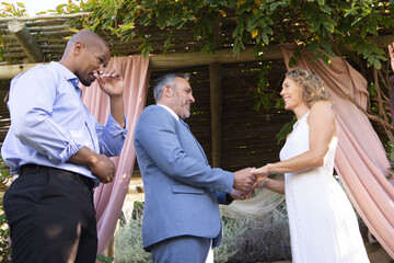 Obraz premium Couple exchanging vows under wood pergola bride white dress groom blue suit guest wiping face left