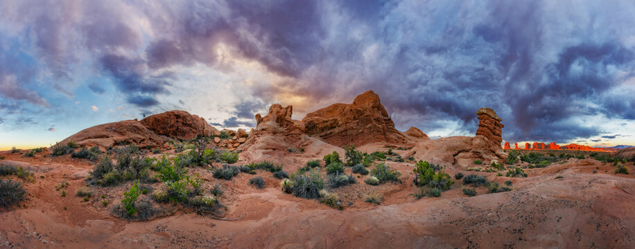 View of red sandstone rock formations and desert landscape under a dramatic stormy sky in Moab, Utah, United States.
