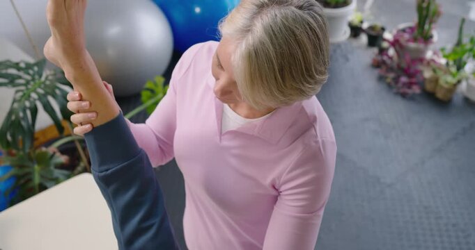 Female therapist lifting and guiding raised patient leg on treatment table, assessing hamstring