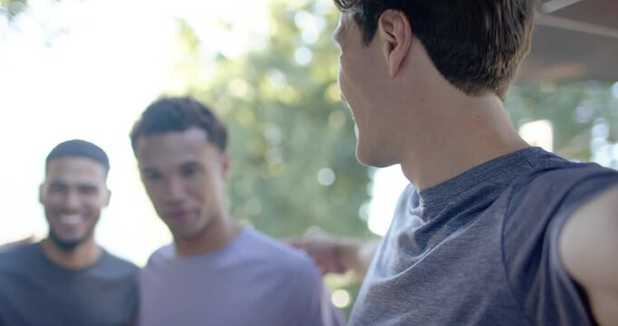 Diverse male friends leaning in on porch while selfie-taker calling, extending phone for selfie