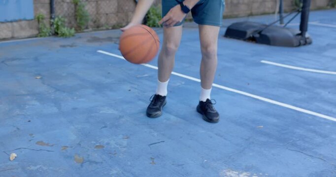 Male teen after crossover picking basketball on blue court, preparing trick, wearing tank, spinning