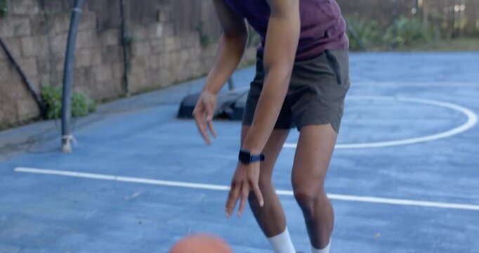 African American man starting on bounce, practicing dribbling basketball and smiling on blue court