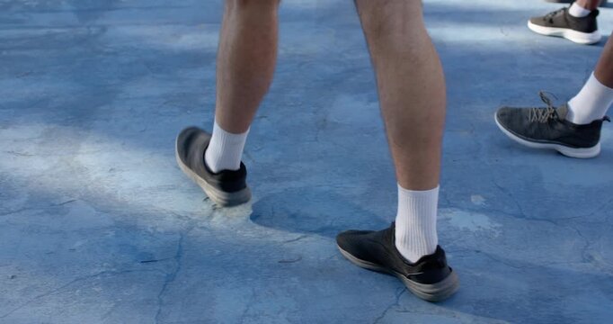 Diverse male friends dribbling basketball walking on blue court after close dribble heading to hoop