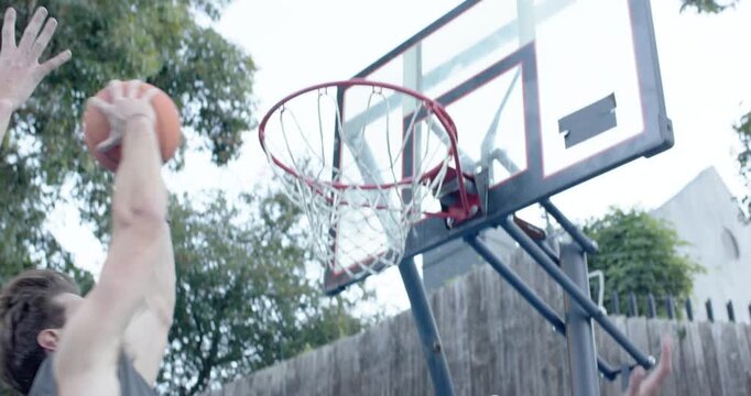 Diverse men on court, one in sportswear spotting rim jumping with basketball to score through hoop