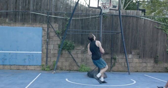 Diverse men playing backyard hoop, shooter in black tank dribbling past defender, jumping for layup