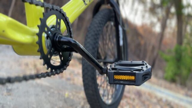 Bicycle drivetrain with crankset and pedal shown in close-up beside a rural road during daylight, presenting cycling mechanics with a dynamic and professional atmosphere.
