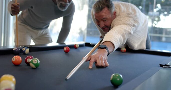 Diverse men playing pool on blue-felt during casual game, one lining up shot, striking cue ball