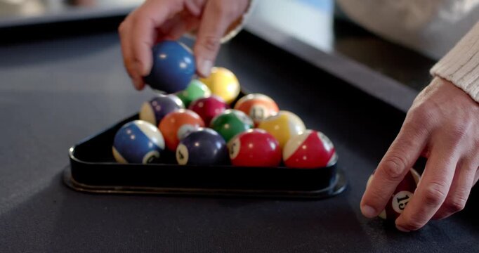 Diverse male players racker in cream sweater placing rack, aligning balls at pool table for break