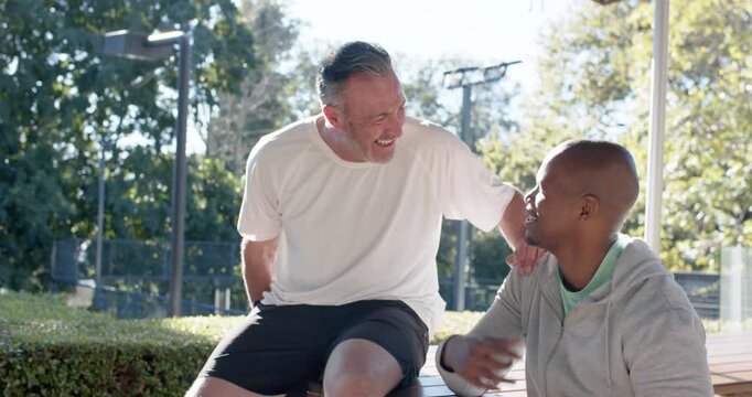 Two male friends African American and light-skinned, placing hand, sparking laughter on park bench