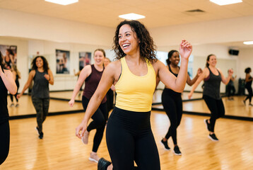 Fototapeta premium Smiling young woman leading an energetic group dance class in a bright studio