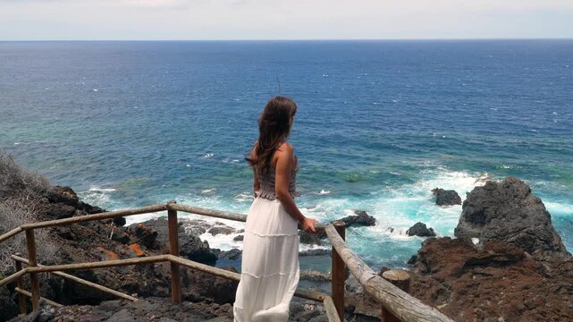 Woman watching the ocean waves from a volcanic cliff viewpoint